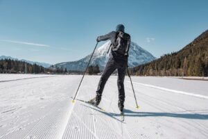 Hiihtäjä tasatyönnössä lumisella ladulla vuoristomaisemassa